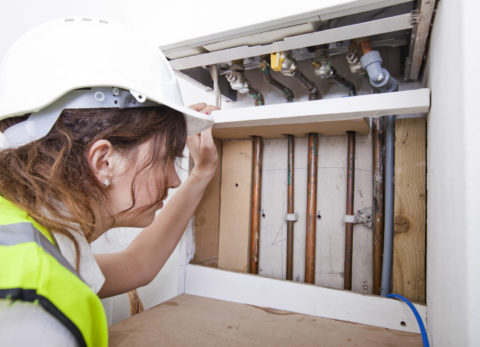 Female plumber examining pipes of central heating boiler