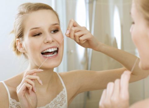 woman looking in the mirror flossing her teeth