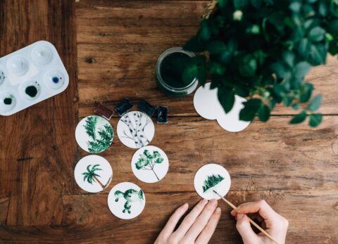 woman painting botanicals on white discs