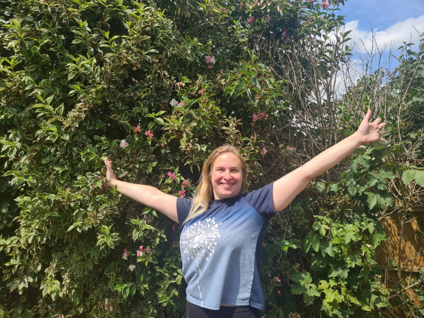 woman in green space with arms up, smiling