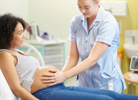 student midwife with pregnant woman on a couch, student is palpating the woman's abdomen
