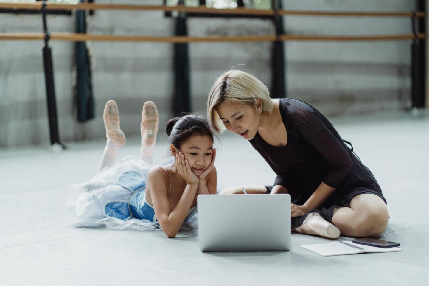mum and daughter kneeling on the floor, daughter is in ballet clothes, they are looking at a laptop