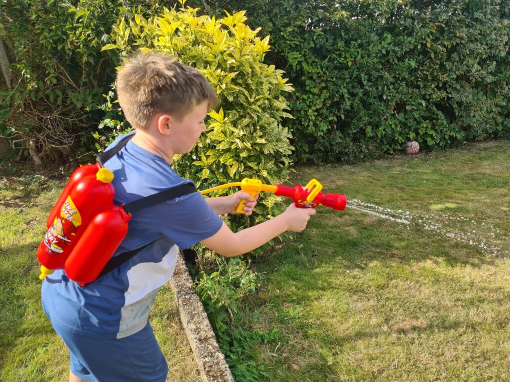 boy playing with water sprayer in garden with dog