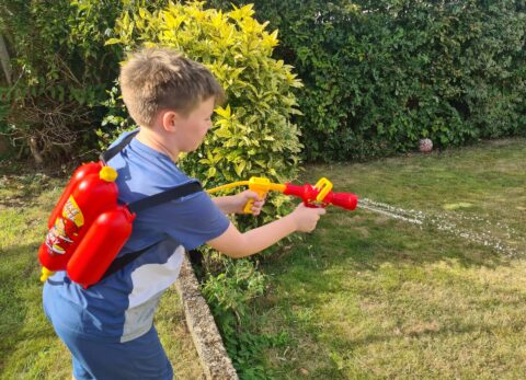 boy playing with water sprayer in garden with dog